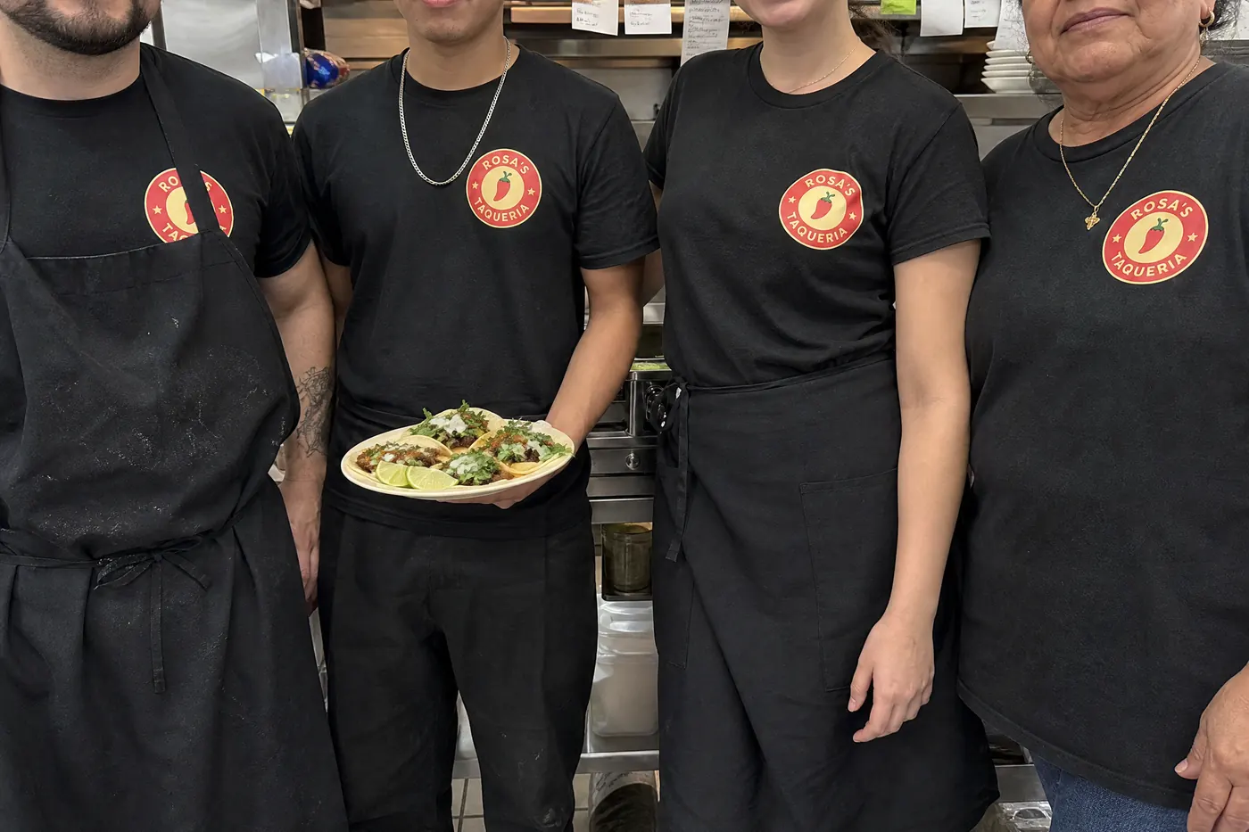 Restaurant staff at the kitchen pass in matching black Rosa's Taqueria shirts
