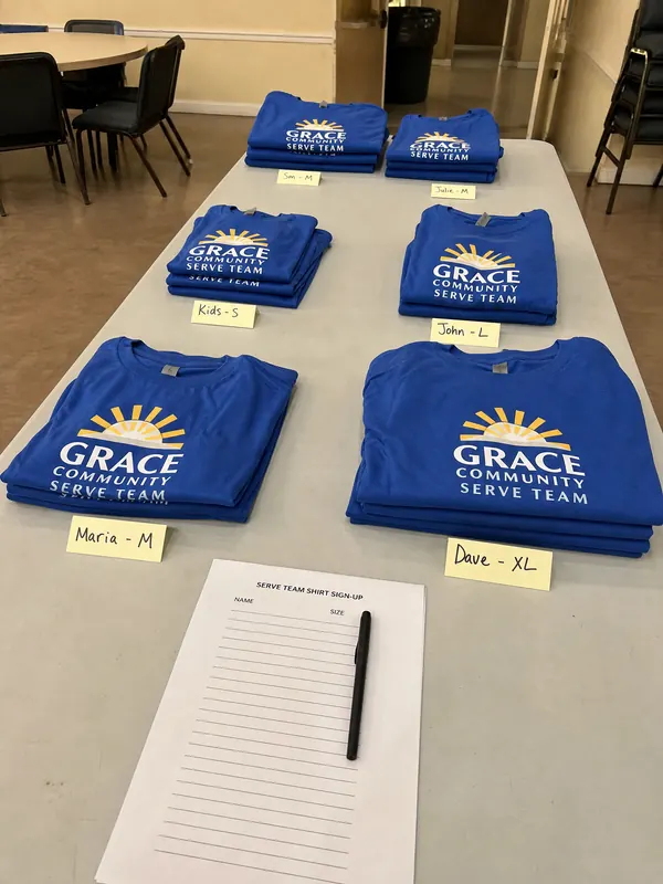 Blue Grace Community Serve Team shirts sorted by size with name notes on a table