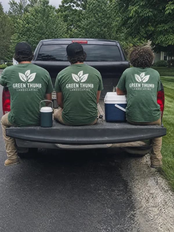 Three landscapers on a truck tailgate, Green Thumb Landscaping printed on the backs of their green shirts