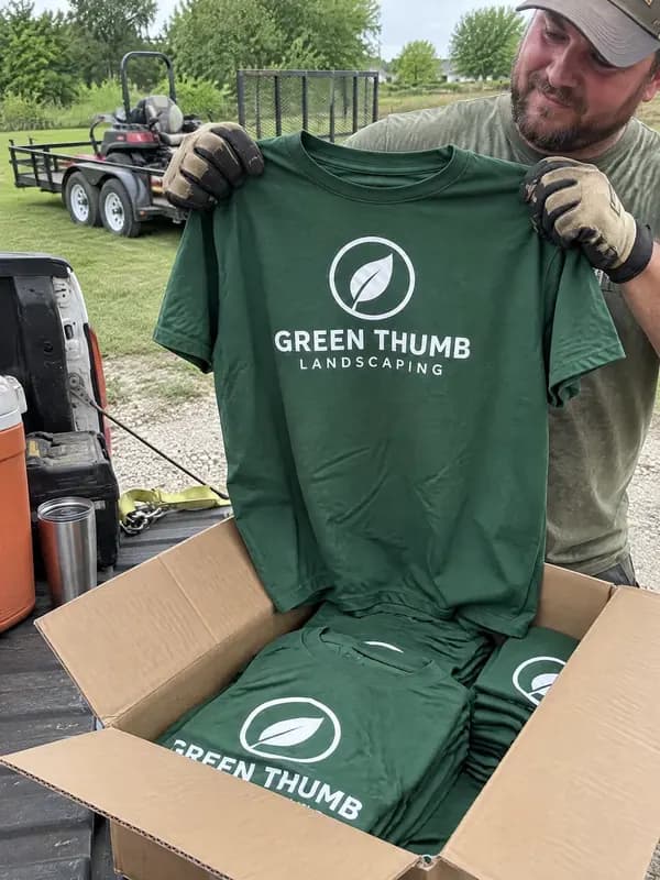 A box of green Green Thumb Landscaping shirts on a truck tailgate