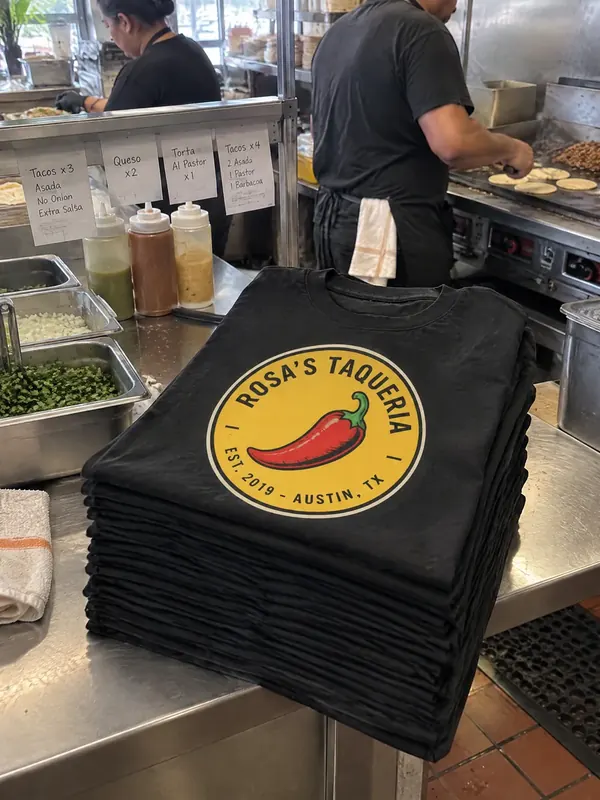A stack of black Rosa's Taqueria shirts on a kitchen counter